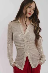 Camisa color beige con lentejuelas, de corte ajustado, cuello camisero y cierre frontal con botones.