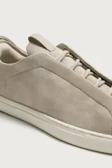 Zapatilla de piel con acabado en serraje de color gris, diseño de cordones ocultos y suela de goma en contraste de color blanco.
