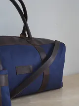 Bolso de lona color verde militar con detalles en cuero marrón. Tiene doble asa de mano y correa de hombro ajustable y extraíble.