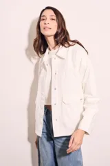 Sobrecamisa color blanco hueso de algodón, con cuello camisero, cierre frontal con botones a presión metálicos, bolsillos de parche en el pecho y bordados florales en los hombros. Corte holgado.