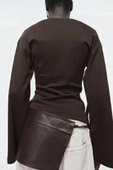 Cinturón tipo falda confeccionado en piel 100% color marrón oscuro, con diseño envolvente y cierre mediante lazada frontal.
