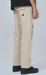 Pantalón cargo de color beige claro, corte recto y holgado, con bolsillos tipo parche en los muslos. Presenta costuras reforzadas en las rodillas y una etiqueta rectangular negra en el bolsillo derecho.