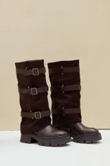 Bota alta de caña ancha, combinada en cuero ecológico y gamuza color marrón, con suela track gruesa y tres tiras horizontales con hebillas metálicas.