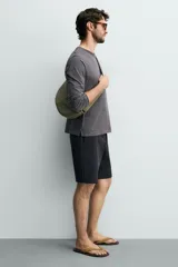 Bolso de hombro de nylon color negro, con diseño curvo y cierre de cremallera en el compartimento principal. Cuenta con asa ajustable para llevar al hombro y bolsillo interior con cierre.