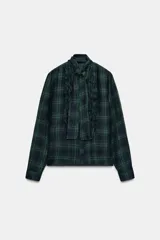 Blusa de manga larga con estampado de cuadros escoceses en tonos verde oscuro y azul marino. Presenta cuello redondo con un pañuelo incorporado que se anuda, y volantes verticales en el frente.