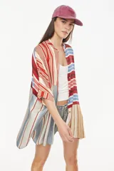 Vestido camisero corto con diseño de paneles combinados en distintos patrones de rayas verticales y horizontales, en tonos rojo, azul, beige y blanco. Posee cuello mao, cierre frontal con botones y mangas cortas caídas.