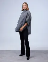 Poncho de tejido soft con estampado de cuadros, cuello alto y cierre frontal parcial. Presenta diseño holgado con mangas amplias y bolsillos laterales.