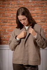 Campera de lana con estampado de cuadros pequeños en tonos marrones y beige. Presenta un cuello de pana en color marrón oscuro, cierre frontal con cremallera oculta por una solapa con botones y mangas largas con puños abotonados.