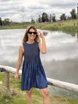 Vestido corto sin mangas de denim azul, con diseño holgado y detalle de nido de abeja (smock) hecho a mano con costuras en hilo marrón en la parte superior.