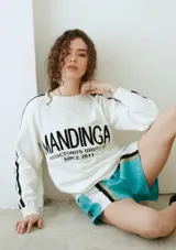 Buzo de punto blanco con líneas negras en las mangas y la inscripción "MANDINGA AUTOCTONOS URUGUAYOS SINCE 2011" en el frente.