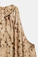 Top de cuello halter con diseño sin mangas, confeccionado en tela fluida con estampado de manchas abstractas. Presenta un cierre en la espalda con abertura y botones.