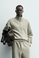 Sudadera de corte relajado confeccionada en tejido técnico interlock de algodón con elasticidad. Presenta cuello subido, cierre frontal con cremallera, manga larga con puños acanalados y bolsillos laterales ocultos en las costuras.