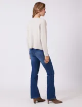 Cardigan tejido de punto color beige, con cuello a la base y cierre frontal mediante un botón metálico decorativo. Presenta mangas largas y corte recto.