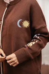 Saco tejido color chocolate con diseño inspirado en la granada, con flores y soles bordados. Presenta cierre frontal con botones, cuello redondo y puños acanalados.