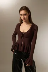 Top de punto color marrón, con cuello redondo amplio, cierre frontal con botones, mangas largas con puños acampanados y detalle de volados en el cuello y el ruedo.