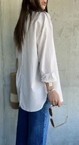Camisa beige con rayas verticales blancas, de corte holgado y largo a la cadera.