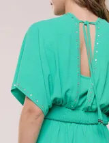 Vestido largo amarillo de corte fluido con escote en V, mangas cortas amplias y apliques de tachas en el escote y puños. Posee cintura elastizada fruncida y falda larga con tajos laterales en el ruedo.