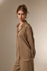 Camisa de poliéster con acabado satinado, de corte holgado, cuello camisero clásico, cierre frontal con botones y mangas largas con puños.