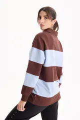 Buzo deportivo sin friza a rayas anchas en tonos blanco y tostado, con cuello polo, escote en V y estampa frontal con la inscripción "California est.1969" en color fucsia. Presenta un corte semi oversize y mangas largas.