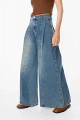 Jean de corte wide leg con pinzas frontales y costuras verticales decorativas. Presenta un diseño de tiro alto con cierre de botón y cremallera, confeccionado en denim de lavado medio.