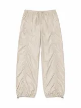 Pantalon estilo parachute de tela técnica con acabado brillante, cintura elástica con cordón ajustable y bajos con cordón elástico. Presenta costuras verticales fruncidas a lo largo de las piernas.