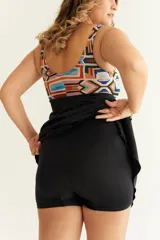 Malla entera con short y vestido negro, con corpiño estampado con motivos geométricos en tonos naranja, celeste y marrón. Presenta un nudo en el centro del escote para regular la profundidad.