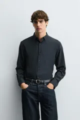 Camisa negra de corte slim fit, con cuello italiano y manga larga con puño abotonado. Cierre frontal de botonadura.
