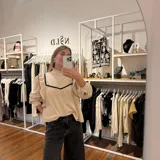 Blusa de lino color beige con cuello alto y volados en el frente y mangas. Presenta detalles de ribetes en terciopelo negro que contrastan con la tela principal. Posee mangas largas con puños abotonados y un diseño romántico y femenino.