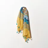 Pashmina rectangular con estampado geométrico en tonos amarillo, azul, celeste y blanco. Tiene flecos con borlas en los extremos.