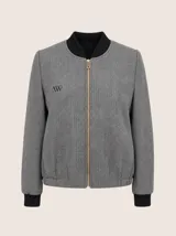 Chaqueta tipo bomber de lana con estampado de espiga en tonos grises. Presenta cuello, puños y ruedo en tejido elástico negro, cierre frontal dorado y bordado sutil en el pecho.
