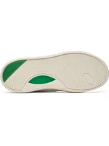 Championes Under Armour modelo UA W Flex, color blanco con detalles en verde. Presenta parte superior de cuero sintético con perforaciones en la puntera, panel lateral ovalado con la inscripción de la marca en dorado, talón acanalado verde y entresuela de goma color marfil con detalle verde.