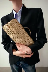 Bolso tipo sobre con diseño trenzado en color dorado. Cuenta con asa de mano fija, asa bandolera extraíble, bolsillo interior y cierre mediante solapa con imán.