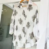 Camisa blanca con estampado damasco verde militar, de corte oversize, manga larga y botones frontales.