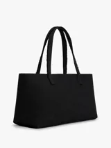 Cartera tipo tote de Tommy Jeans confeccionada en denim de algodón color negro. Presenta un diseño rectangular con asas superiores y una cadena metálica decorativa en el frente. Incluye el logo de la marca bordado en el centro.