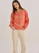 Camisa voluminosa de algodón con mangas amplias y abullonadas que se ajustan en los puños. Tiene calce suelto, hombro caído, cuello redondo y cierre frontal con botones. Presenta estampado geométrico en tonos mostaza y beige.