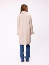 Gabardina de corte clásico en color azul marino, con cierre frontal de botones, cuello camisero y bolsillos laterales. Presenta un diseño minimalista con un pequeño bordado en el pecho.