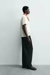 Camiseta de corte relajado (relaxed fit) color blanco hueso, con cuello redondo, manga corta y bolsillo plastrón en el pecho. Presenta un bordado pequeño y contrastante de una palmera en el área del bolsillo.