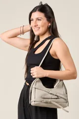 Cartera bandolera de ecocuero texturado color gris claro, con correa ajustable y detalles de hebillas decorativas.