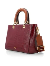 Cartera de mano de estructura rígida con textura símil cocodrilo en color bordó, con manijas superiores cortas en tono tostado y herrajes metálicos dorados.