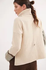 Polera de calce relajado con cuello alto, confeccionada en lana. Presenta un diseño bicolor con cuerpo en gris claro y mangas con estampado jacquard de arabescos en tonos tierra y negro. Incluye detalle de costura central vertical en el frente.