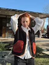 Chaleco negro con interior de corderito, con detalles en color naranja y ribeteado en marrón.