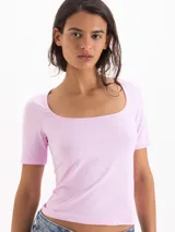 Top de silueta ajustada y largo hasta la cadera, confeccionado en tejido de punto liso color rosado. Presenta un escote ovalado profundo y mangas cortas de calce ceñido.