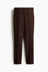 Pantalón de punto elástico color marrón, de corte ajustado, con pliegues frontales cosidos y cierre en los bajos.