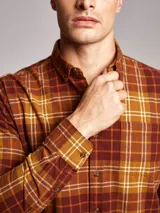 Camisa de manga larga confeccionada en franela de algodón, con diseño de cuadros en tonos marrones, mostaza y blanco. Presenta cuello con botones, cierre frontal abotonado y bolsillo en el pecho.
