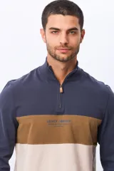 Remera polo de manga larga con diseño de bloques de color en azul marino, marrón y beige. Presenta cuello alto con cierre frontal parcial y estampa frontal con el logo de la marca.