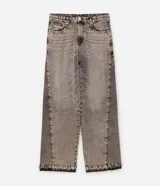 Pantalón jean de corte super baggy con piernas amplias, confeccionado en denim de algodón. Presenta un acabado lavado grisáceo, ruedo desflecado y detalle de costura frontal tipo nesga.