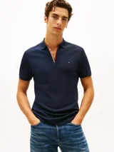Chomba azul marino Tommy Hilfiger de manga corta y corte regular, confeccionada en algodón. Cuenta con cuello polo, cierre de cremallera parcial con detalles tricolor en el interior y logo bordado en el pecho.