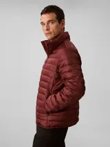 Campera puffer ligera de Calvin Klein, color bordó, con acolchado de canales horizontales, cuello alto y cierre frontal de cremallera. Presenta un diseño minimalista con logo de la marca en el pecho.