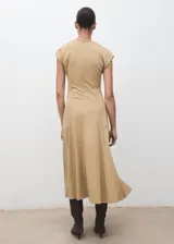 Vestido midi de manga corta en color beige, con cuello en V, diseño evasé, costuras decorativas visibles y cierre de cremallera en la parte posterior.