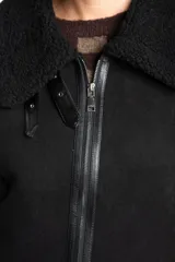 Chaleco estilo gamulán de color negro, con interior y detalles de corderito sintético. Presenta cierre frontal, cuello solapa y bolsillos laterales.